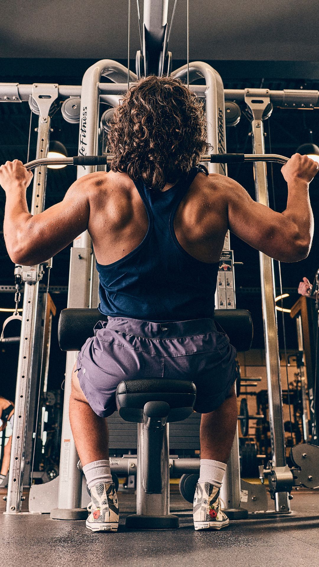 Man performing a lat pulldown on a cable machine at Gold’s Gym Greeley with another member training on a cable station in the background