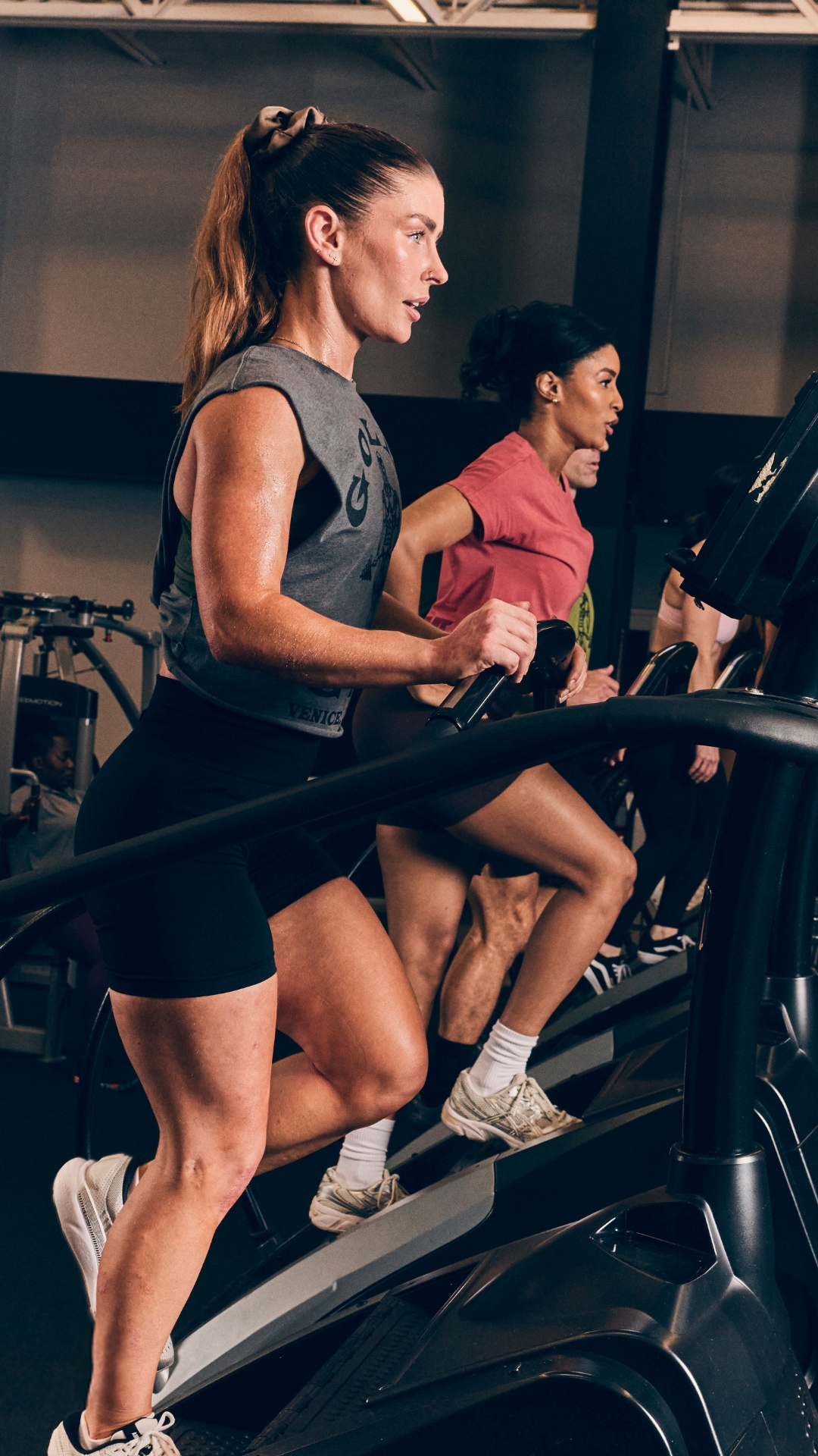Two women training on stair climber machines at Gold’s Gym Greeley focused on intense cardio in a serious training environment