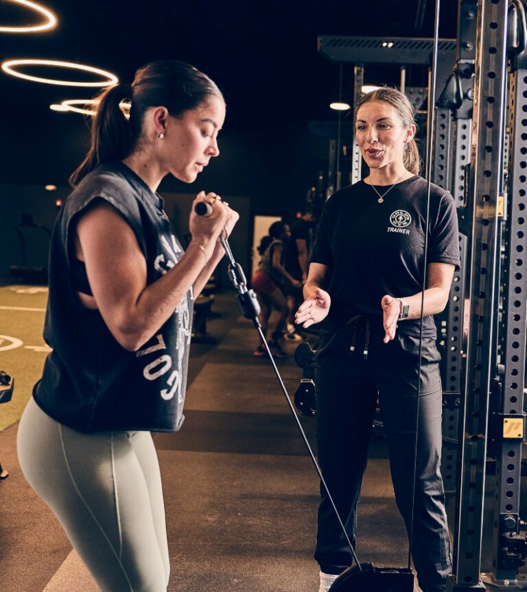 Member working with a personal trainer on a cable exercise at Gold’s Gym Longmont, highlighting one-on-one coaching in a serious training environment