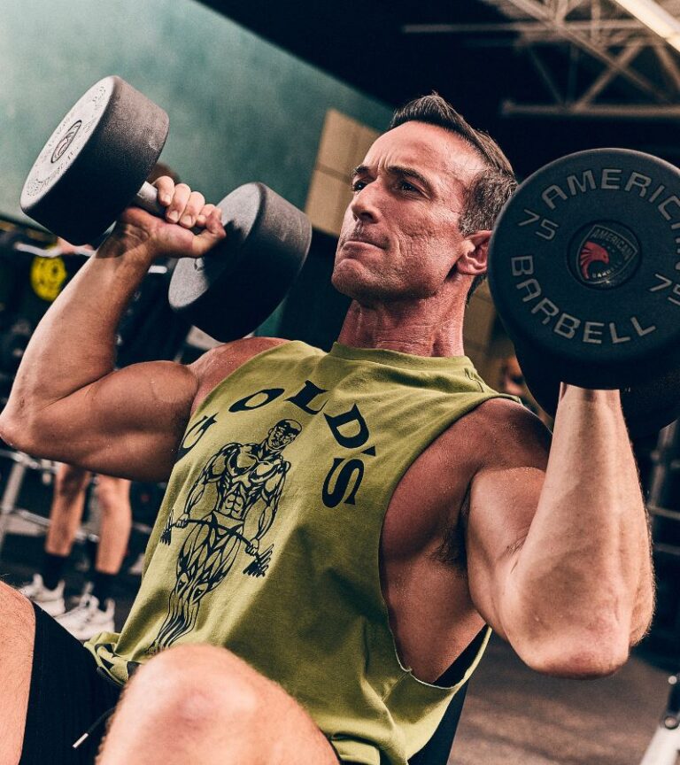 Man performing a seated dumbbell shoulder press at Gold's Gym, highlighting strength training at our Colorado fitness centers.